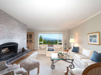 Experience breathtaking panoramic views from this stunning living room, featuring a cozy brick fireplace and ample natural light pouring in through large windows.