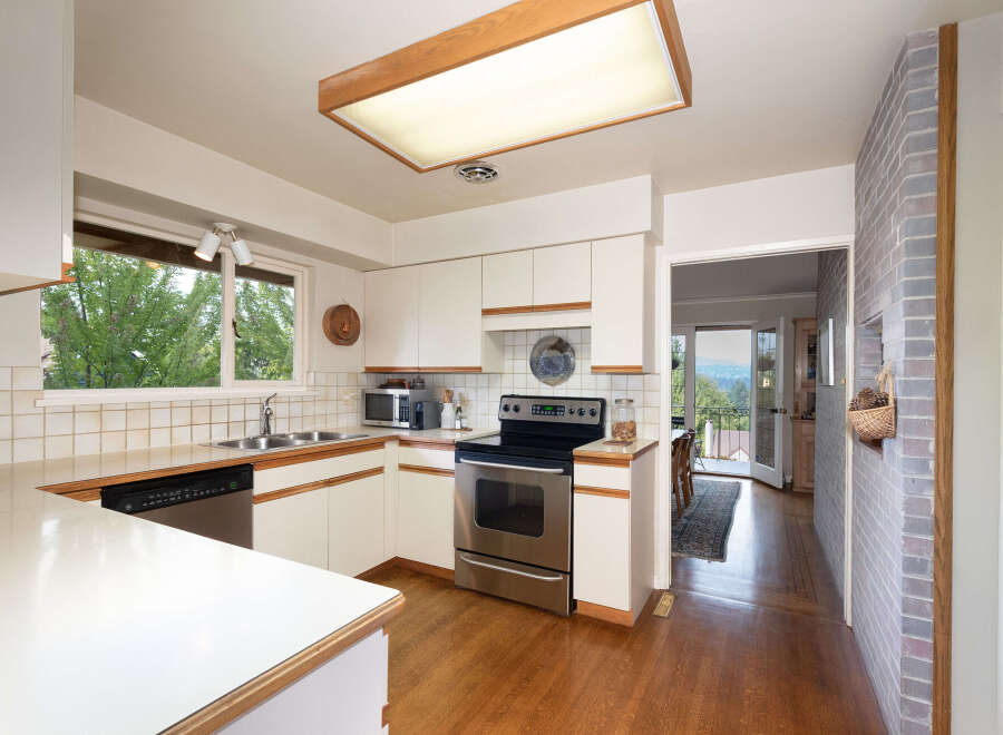 This charming kitchen features white cabinetry, a tiled backsplash, and a stainless steel range.