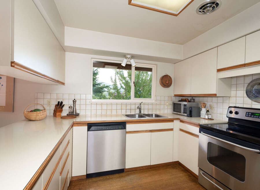This charming kitchen features a double-basin sink beneath a large window offering a view of lush greenery.