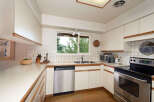 This charming kitchen features a double-basin sink beneath a large window offering a view of lush greenery.