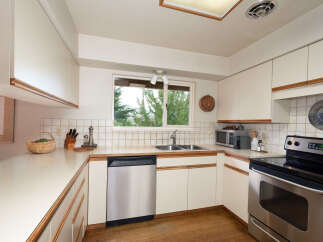 This charming kitchen features a double-basin sink beneath a large window offering a view of lush greenery.