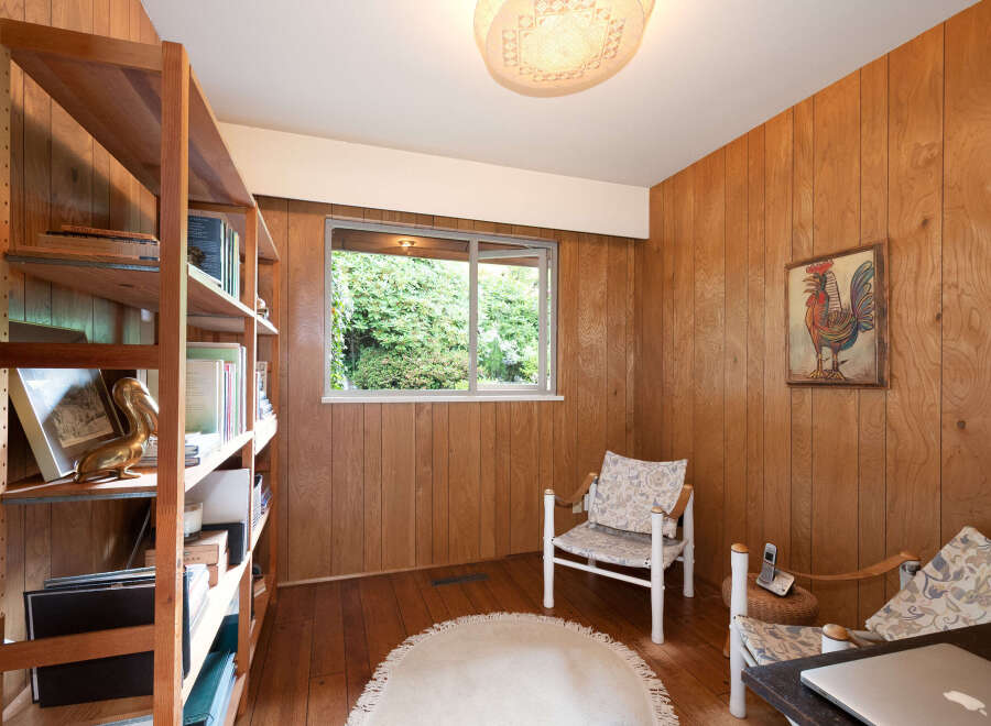 This cozy room features warm wood paneling and a large window offering a lush green view.