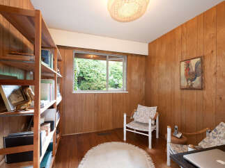 This cozy room features warm wood paneling and a large window offering a lush green view.