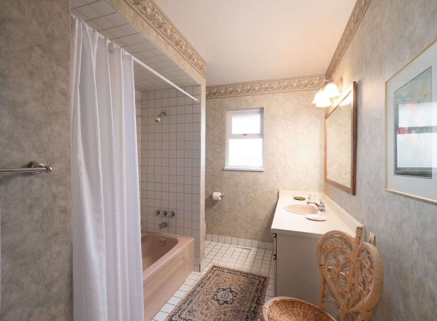 This bathroom features a classic design with a pink bathtub and shower combination, complemented by a white tiled shower surround.