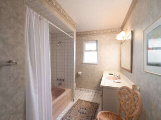 This bathroom features a classic design with a pink bathtub and shower combination, complemented by a white tiled shower surround.