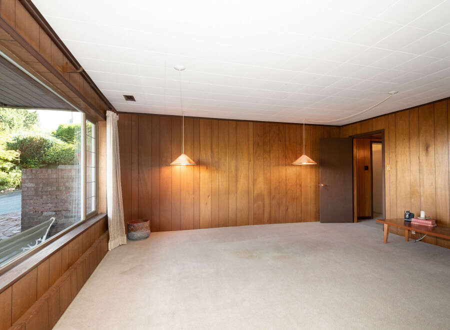 Step into a retro-inspired living space featuring warm wood paneling and a large picture window that floods the room with natural light.