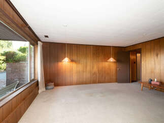 Step into a retro-inspired living space featuring warm wood paneling and a large picture window that floods the room with natural light.
