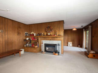 Step into this charming living room featuring warm wood-paneled walls and a cozy fireplace, perfect for gathering.