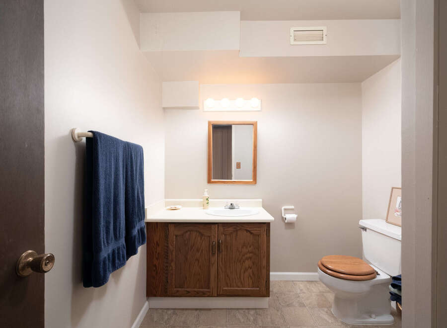 This charming bathroom features a wooden vanity with a white countertop and sink, complemented by a wooden-framed mirror and a vanity light.