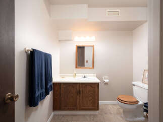 This charming bathroom features a wooden vanity with a white countertop and sink, complemented by a wooden-framed mirror and a vanity light.