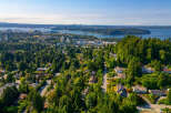 Discover this stunning aerial view of a lush, green neighborhood nestled against a backdrop of a vibrant cityscape and sparkling blue water.