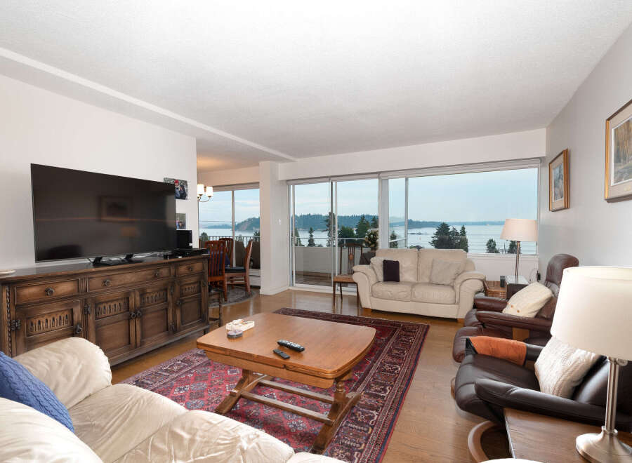 Experience breathtaking water and mountain views from this stunning living room, featuring a large flat-screen TV and a beautiful wooden media console.