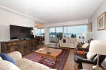 Experience breathtaking water and mountain views from this stunning living room, featuring a large flat-screen TV and a beautiful wooden media console.