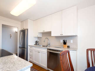 This modern kitchen features sleek white cabinetry and granite countertops, complemented by a stainless steel refrigerator and dishwasher.