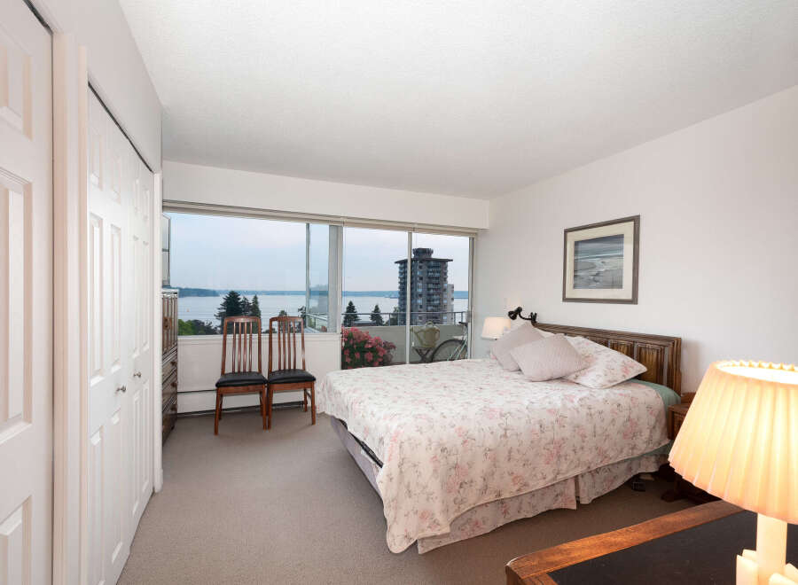 Experience breathtaking water and city views from this serene bedroom, featuring a comfortable queen-size bed with a floral comforter.