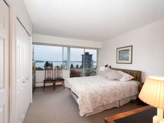 Experience breathtaking water and city views from this serene bedroom, featuring a comfortable queen-size bed with a floral comforter.