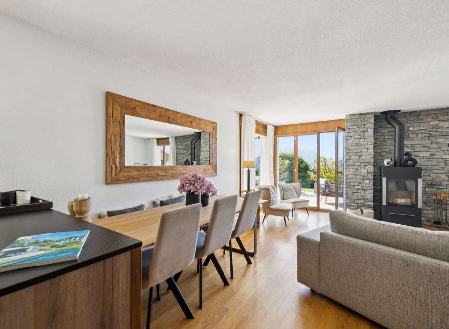 Experience luxurious living in this stunning open-plan space, featuring a modern dining area with a large wooden mirror and a cozy living room centered around a striking stone fireplace.
