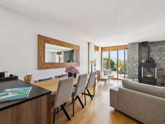 Experience luxurious living in this stunning open-plan space, featuring a modern dining area with a large wooden mirror and a cozy living room centered around a striking stone fireplace.