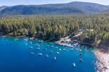 Experience lakeside luxury with this stunning aerial view of a property nestled along a pristine blue lake, surrounded by a dense, verdant forest.