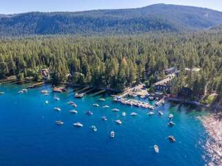 Experience lakeside luxury with this stunning aerial view of a property nestled along a pristine blue lake, surrounded by a dense, verdant forest.