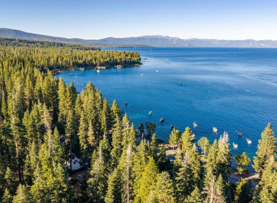 Experience the ultimate lakeside living with this stunning aerial view of a property nestled amidst a lush pine forest, offering direct access to a crystal-clear blue lake.