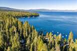 Experience the ultimate lakeside living with this stunning aerial view of a property nestled amidst a lush pine forest, offering direct access to a crystal-clear blue lake.