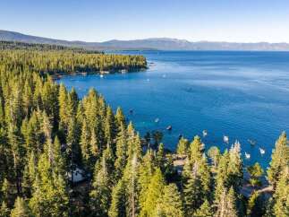 Experience the ultimate lakeside living with this stunning aerial view of a property nestled amidst a lush pine forest, offering direct access to a crystal-clear blue lake.