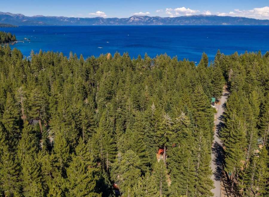 Discover serene living amidst a lush pine forest with breathtaking views of a vast blue lake and distant mountains.