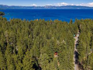 Discover serene living amidst a lush pine forest with breathtaking views of a vast blue lake and distant mountains.