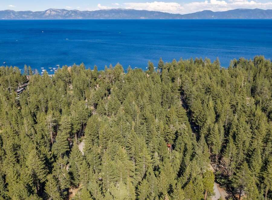 Discover this stunning property nestled amidst a lush pine forest, offering breathtaking views of a vast, blue lake and distant mountains.