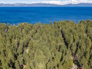 Discover this stunning property nestled amidst a lush pine forest, offering breathtaking views of a vast, blue lake and distant mountains.