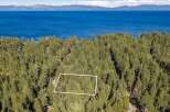 Discover this stunning property nestled amidst a lush pine forest, offering breathtaking views of a vast, blue lake and distant mountains.