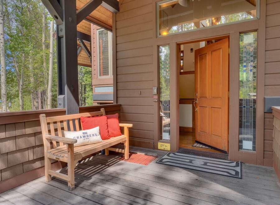 Welcome guests to this charming mountain retreat with a cozy wooden bench and vibrant accent pillows on the porch.