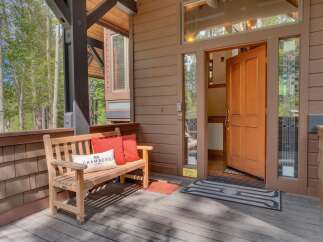 Welcome guests to this charming mountain retreat with a cozy wooden bench and vibrant accent pillows on the porch.