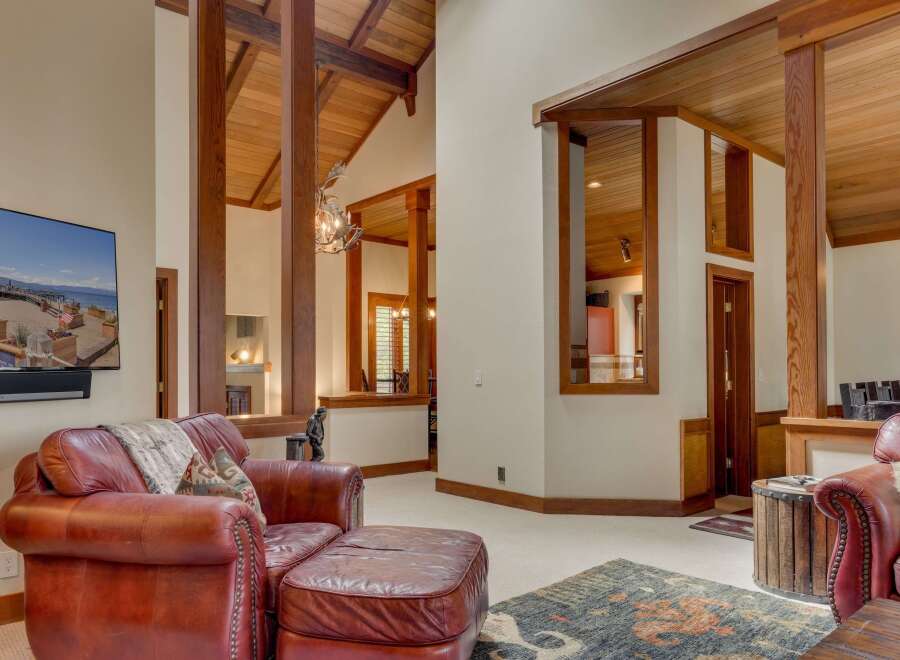 Experience rustic elegance in this spacious living area, featuring soaring vaulted ceilings with exposed wooden beams and a striking antler chandelier.