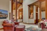 Experience rustic elegance in this spacious living area, featuring soaring vaulted ceilings with exposed wooden beams and a striking antler chandelier.