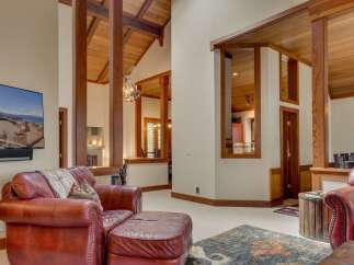 Experience rustic elegance in this spacious living area, featuring soaring vaulted ceilings with exposed wooden beams and a striking antler chandelier.