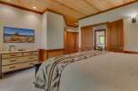 Experience rustic charm in this inviting bedroom, featuring a warm wood-paneled ceiling and a large flat-screen TV mounted above a rustic dresser.