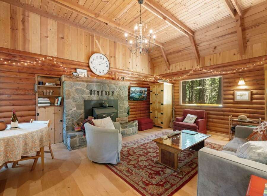 Experience rustic charm in this cozy log cabin living room, featuring a grand stone fireplace and a vaulted wood-paneled ceiling adorned with twinkling string lights.
