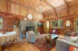 Experience rustic charm in this cozy log cabin living room, featuring a grand stone fireplace and a vaulted wood-paneled ceiling adorned with twinkling string lights.