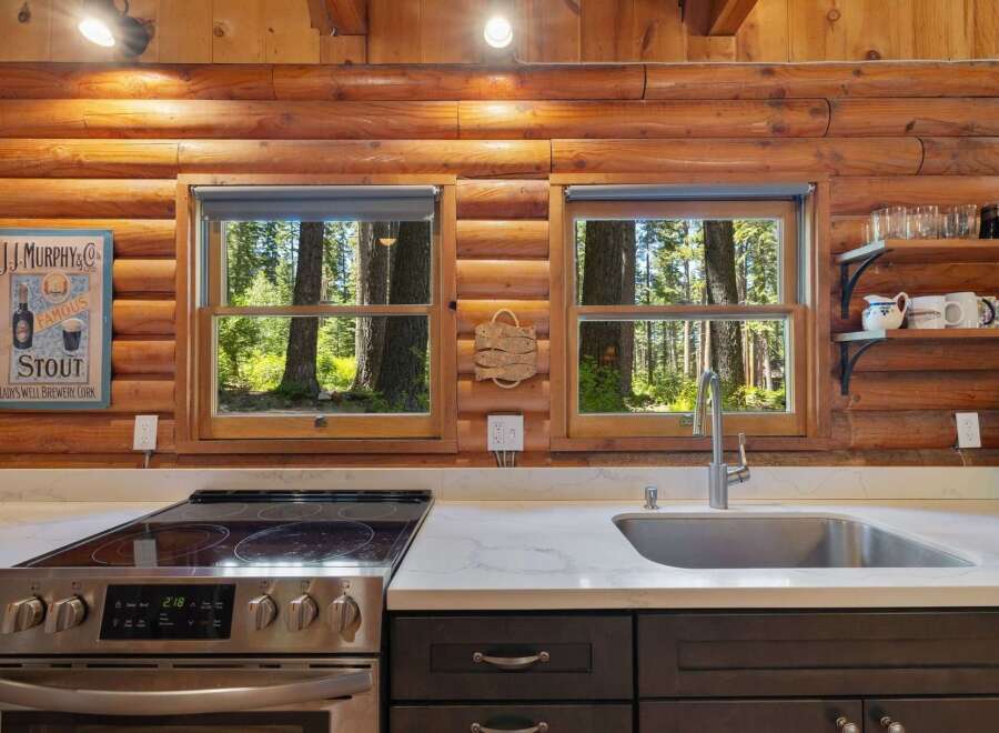 Experience rustic charm in this log cabin kitchen, featuring a modern electric stove and a deep stainless steel sink.