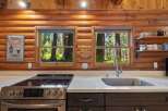 Experience rustic charm in this log cabin kitchen, featuring a modern electric stove and a deep stainless steel sink.