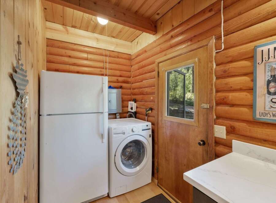 Discover the charm of this rustic log cabin, featuring a convenient laundry area with a full-size refrigerator and a front-loading washing machine.