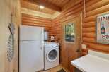 Discover the charm of this rustic log cabin, featuring a convenient laundry area with a full-size refrigerator and a front-loading washing machine.