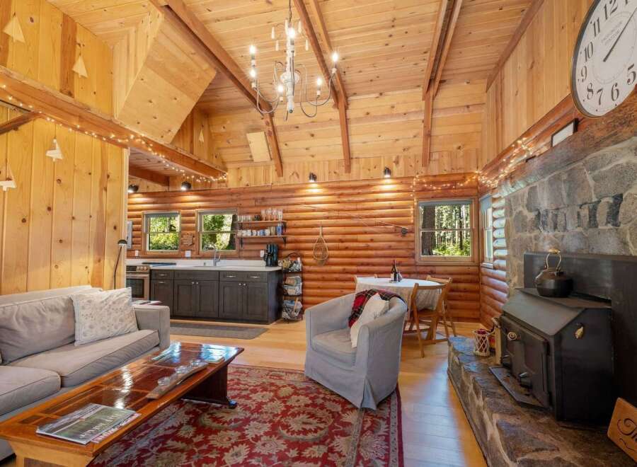 Experience rustic charm in this cozy log cabin living space, featuring a stone fireplace and a well-equipped kitchen.