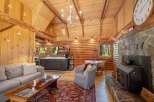 Experience rustic charm in this cozy log cabin living space, featuring a stone fireplace and a well-equipped kitchen.