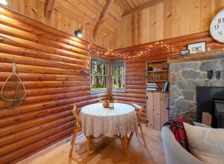 Experience rustic charm in this cozy log cabin dining area, featuring a quaint table set for two and illuminated by whimsical string lights.