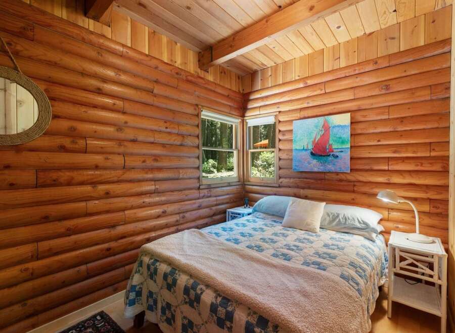 Experience rustic charm in this cozy log cabin bedroom, featuring a comfortable bed adorned with a classic blue and white quilt and a plush throw.