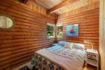 Experience rustic charm in this cozy log cabin bedroom, featuring a comfortable bed adorned with a classic blue and white quilt and a plush throw.