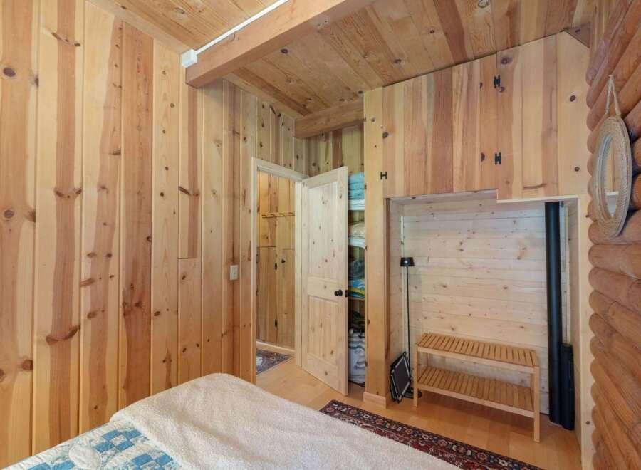 Experience rustic charm in this cozy cabin bedroom, featuring warm wood paneling throughout and a vaulted wood-beamed ceiling.